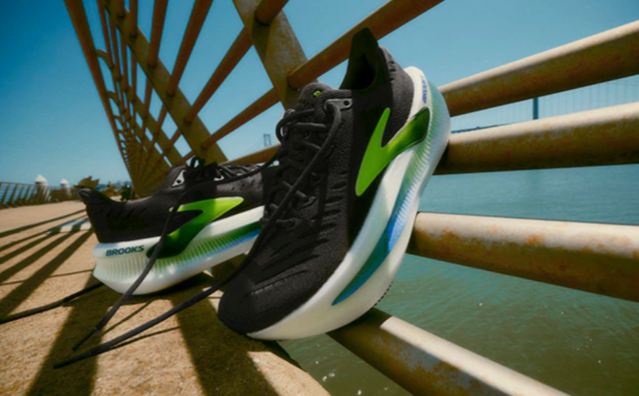 Black running shoes with neon green accents resting on a rusted railing by the water on a sunny day.