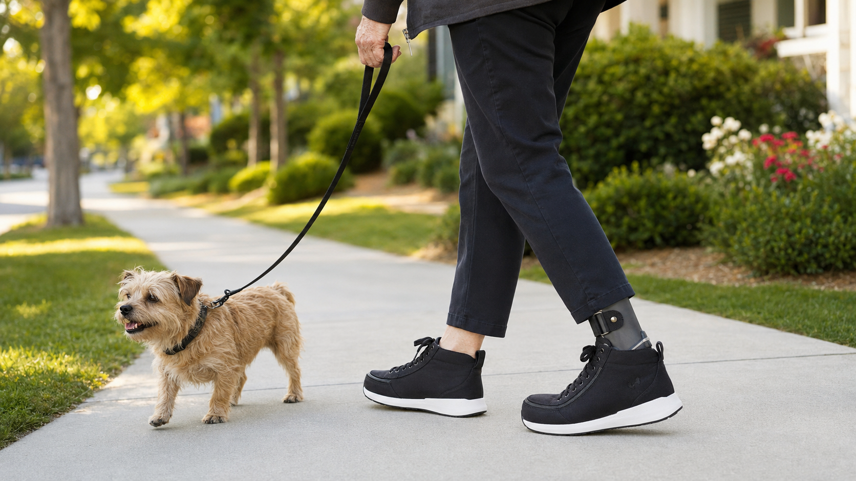 5989 - Rejuva Sole™ Person walks a small tan dog on a leash along a sunny suburban sidewalk.