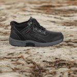 Black hiking shoe on a rugged, sandy ground; sturdy sole and laces visible, outdoors scenario