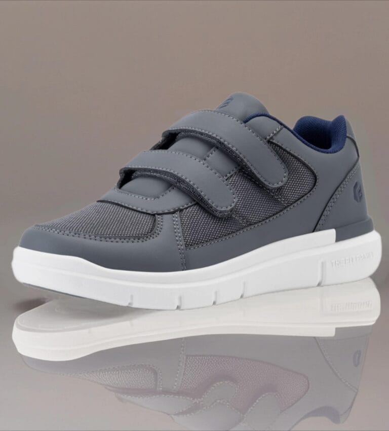Gray athletic sneaker with two Velcro straps and a white sole, shown from the side on a reflective surface.