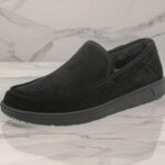 Black suede slip-on loafer with plush lining and chunky rubber sole, shown on a marble surface from the side.