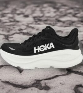 Bazaart_20260724_031528_925 - Rejuva Sole™ Black HOKA running shoe with a thick white sole on a rocky surface, side view