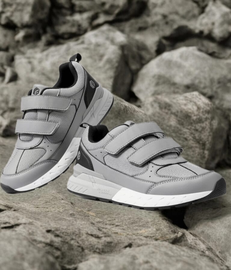 Pair of gray athletic sneakers with Velcro straps resting on a rocky surface.