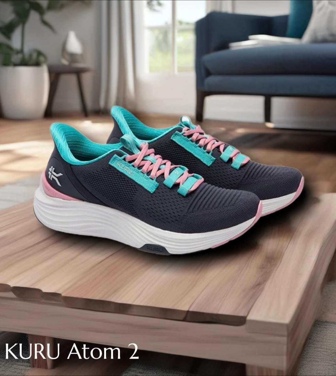 Pair of navy running shoes with turquoise trim and pink laces on a wooden coffee table in a living room,'KURU Atom 2' text visible on the image.